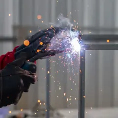 Spawacz w rękawicach tworzy jasny łuk elektryczny, sypiąc iskrami podczas łączenia metalowych elementów.