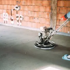 Pracownik wygładza wylewkę samopoziomującą za pomocą mechanicznej pacy. Sprawdź, jaka jest wylewka samopoziomująca cena robocizny.