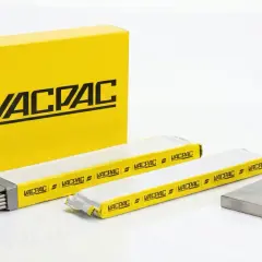 Żółte opakowanie Vacpac zawiera różne rodzaje elektrod spawalniczych. Obok leżą dwie paczki elektrod i metalowy kolanko.