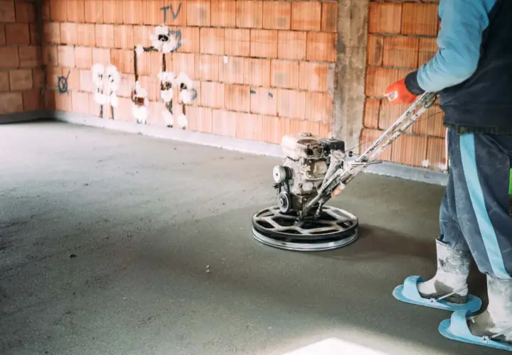 Pracownik wygładza wylewkę samopoziomującą za pomocą mechanicznej pacy. Sprawdź, jaka jest wylewka samopoziomująca cena robocizny.