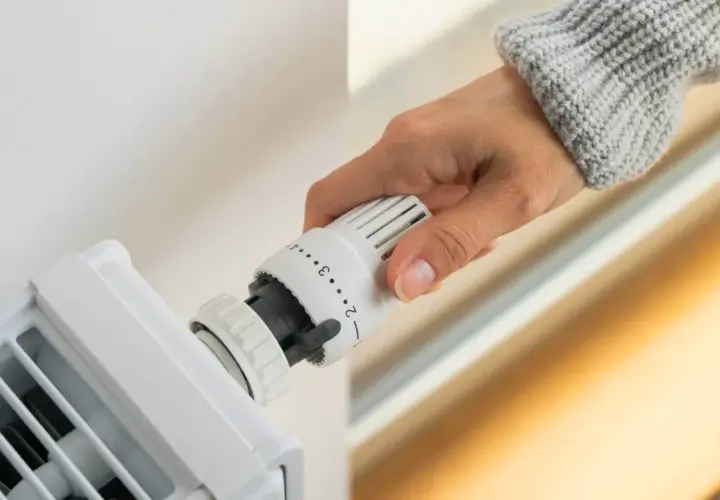 Dłoń reguluje termostat grzejnika, ustawiając optymalną temperaturę w pomieszczeniu.