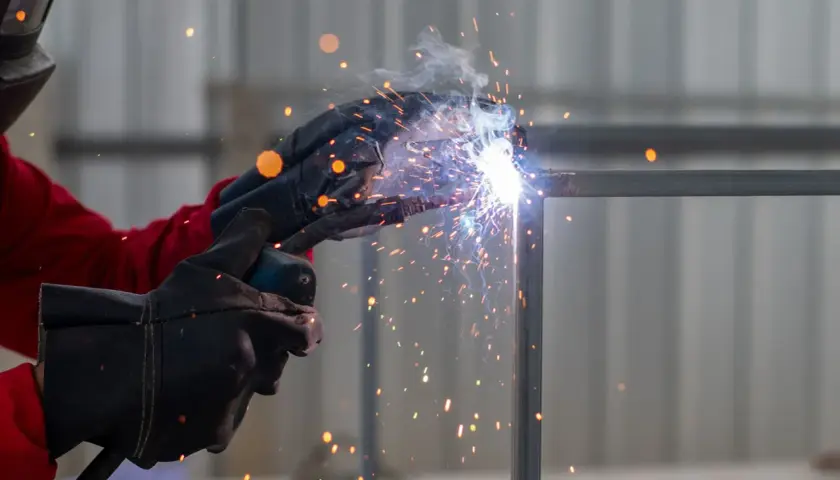 Spawacz w rękawicach tworzy jasny łuk elektryczny, sypiąc iskrami podczas łączenia metalowych elementów.
