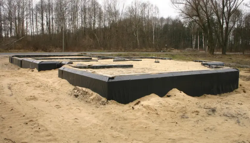 Fundament domu w piasku, otoczony czarną folią. To dopiero początek budowy, przyszły dom otacza opaska wokół domu.