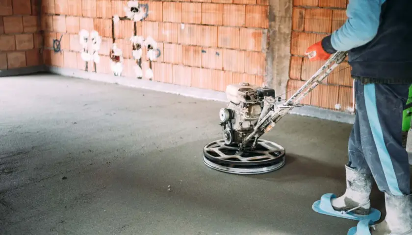 Pracownik wygładza wylewkę samopoziomującą za pomocą mechanicznej pacy. Sprawdź, jaka jest wylewka samopoziomująca cena robocizny.