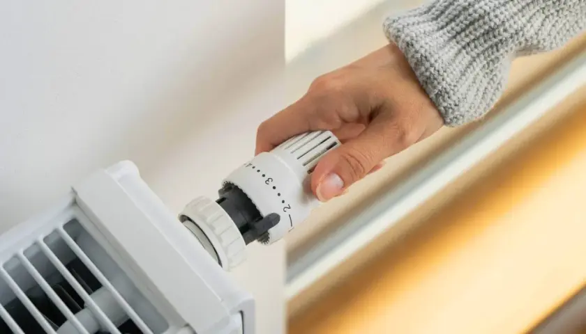 Dłoń reguluje termostat grzejnika, ustawiając optymalną temperaturę w pomieszczeniu.