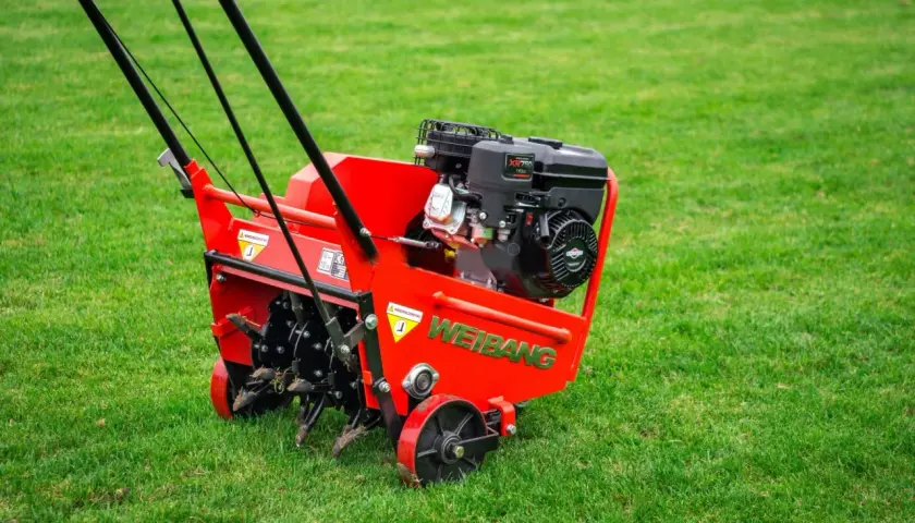 Czerwony aerator Weidemann na zielonej trawie. Idealny czas na aerację trawnika, gdy jest wilgotna i gotowa na odżywienie.