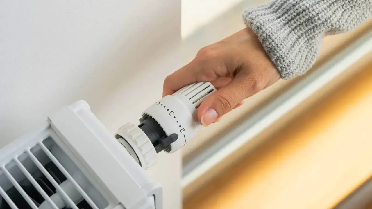 Dłoń reguluje termostat grzejnika, ustawiając optymalną temperaturę w pomieszczeniu.