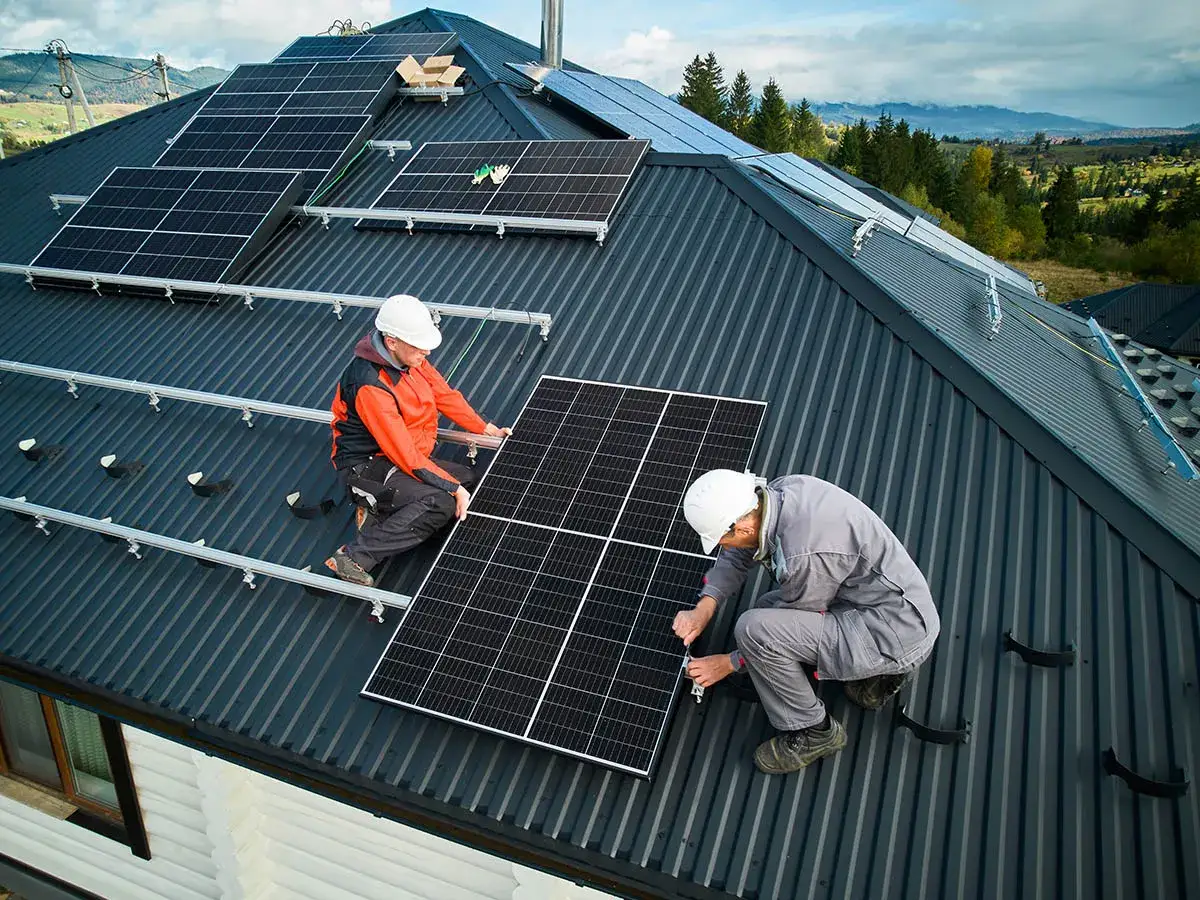 Dwóch mężczyzn montuje panele fotowoltaiczne na dachu. Instalacja PV w malowniczej okolicy.