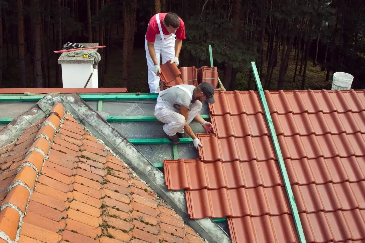 Dwaj dekarze układają nowe dachówki. Widać łaty i kontrłaty rozstaw, które stanowią podstawę dla nowego pokrycia.